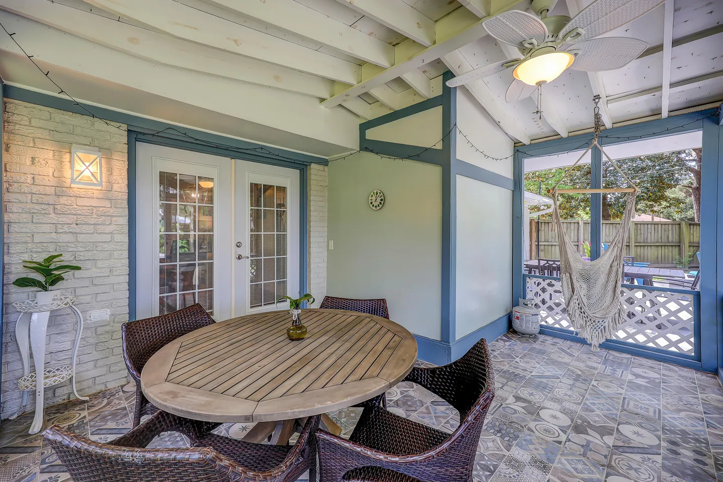 Screened-in porch featuring a round wooden dining table with wicker chairs, decorative tile flooring, and a hanging hammock chair.