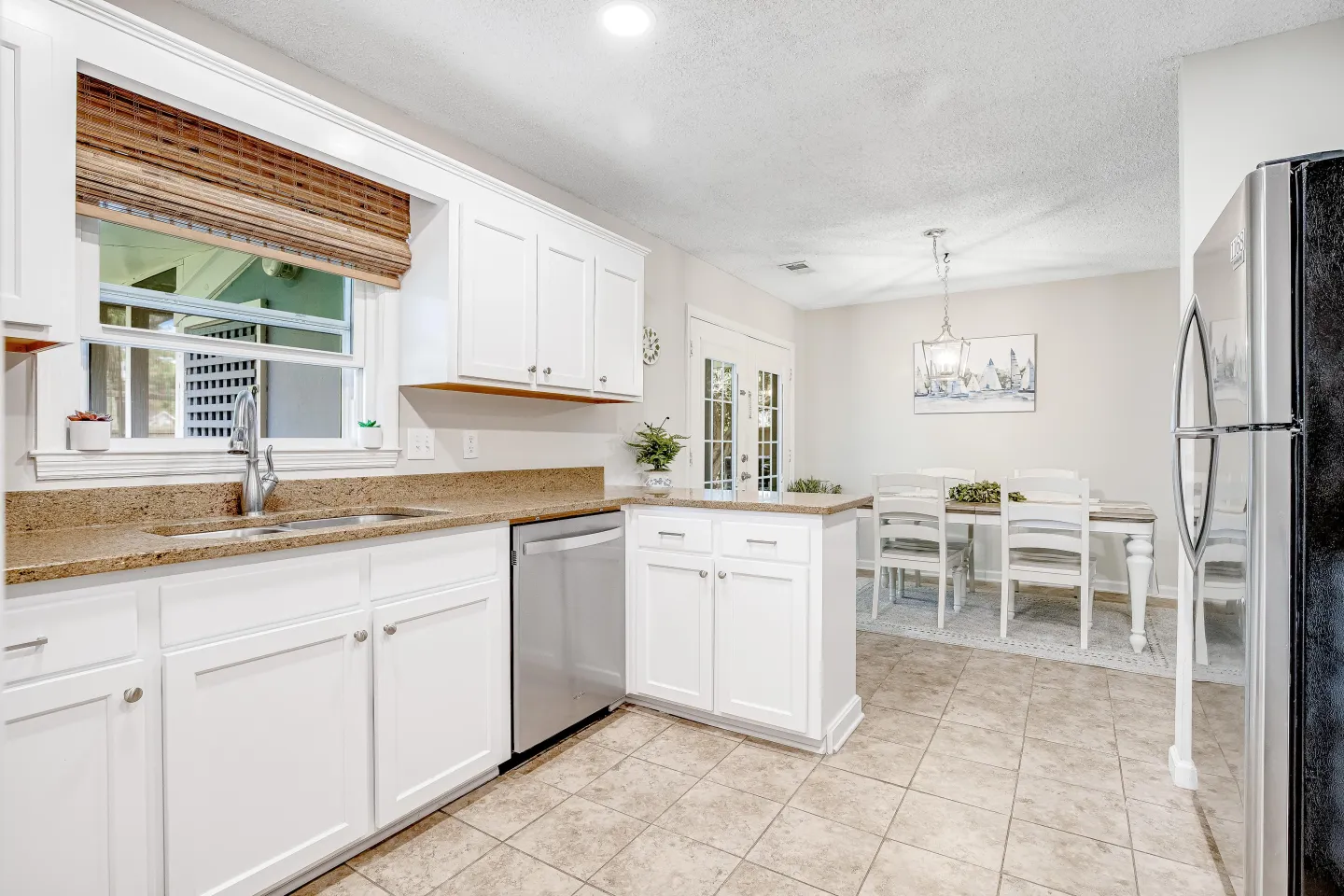 Kitchen with white cabinetry, brown countertops, and stainless steel appliances opening into an adjacent dining area.