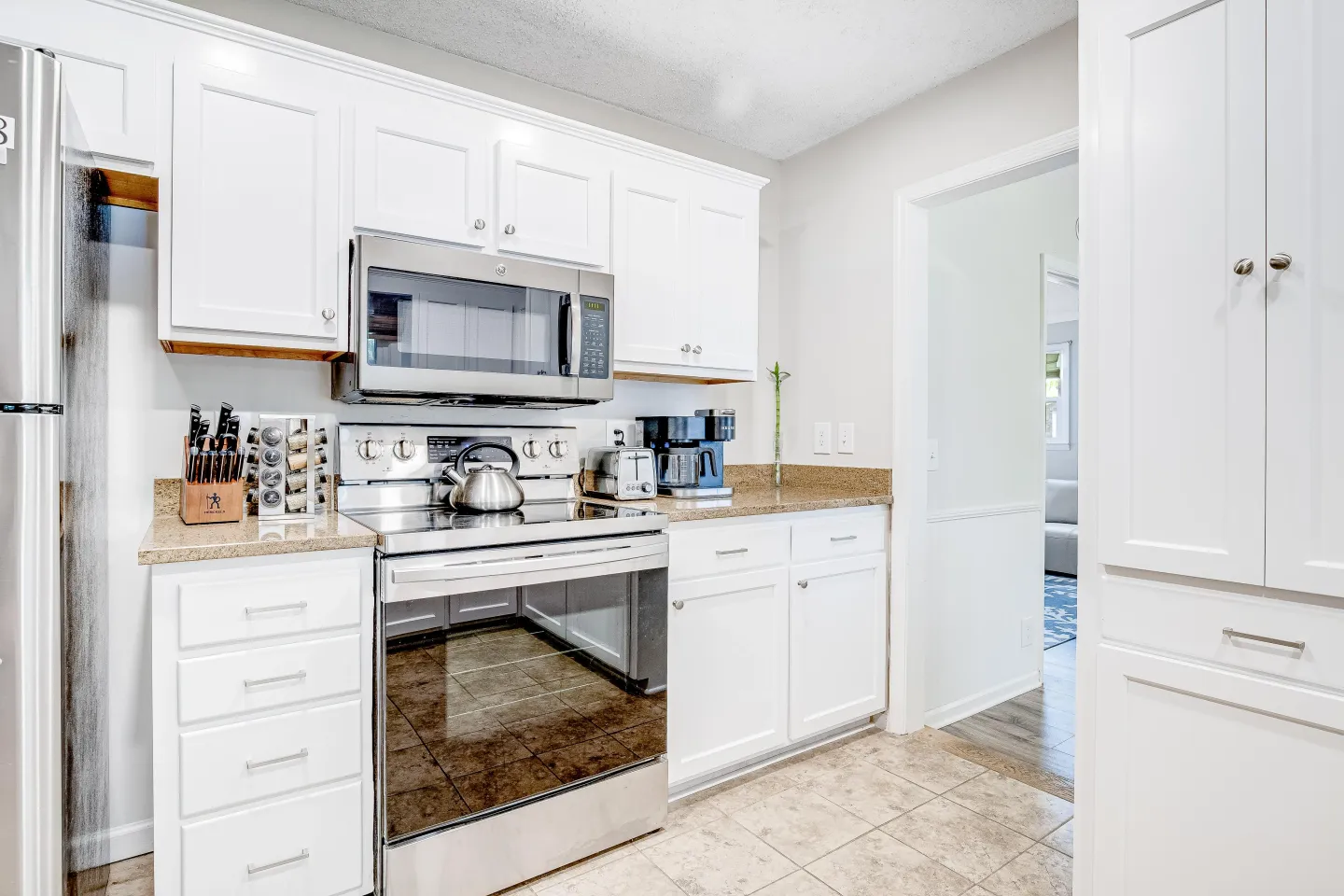 Kitchen with white cabinetry, speckled countertops, stainless steel electric range, and mounted microwave.