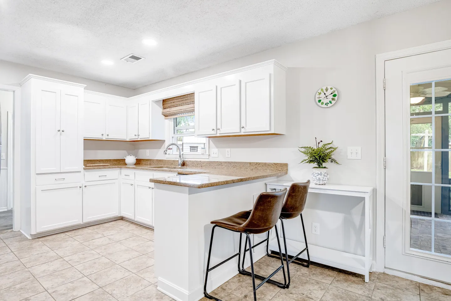 Bright kitchen featuring white cabinetry, beige countertops, tiled floors, and a breakfast bar with two leather-style barstools.
