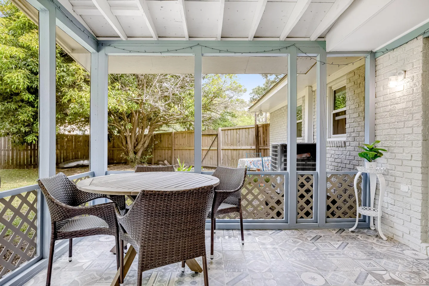 Screened-in porch featuring a round table with woven wicker chairs, tiled flooring, and views of a fenced backyard.