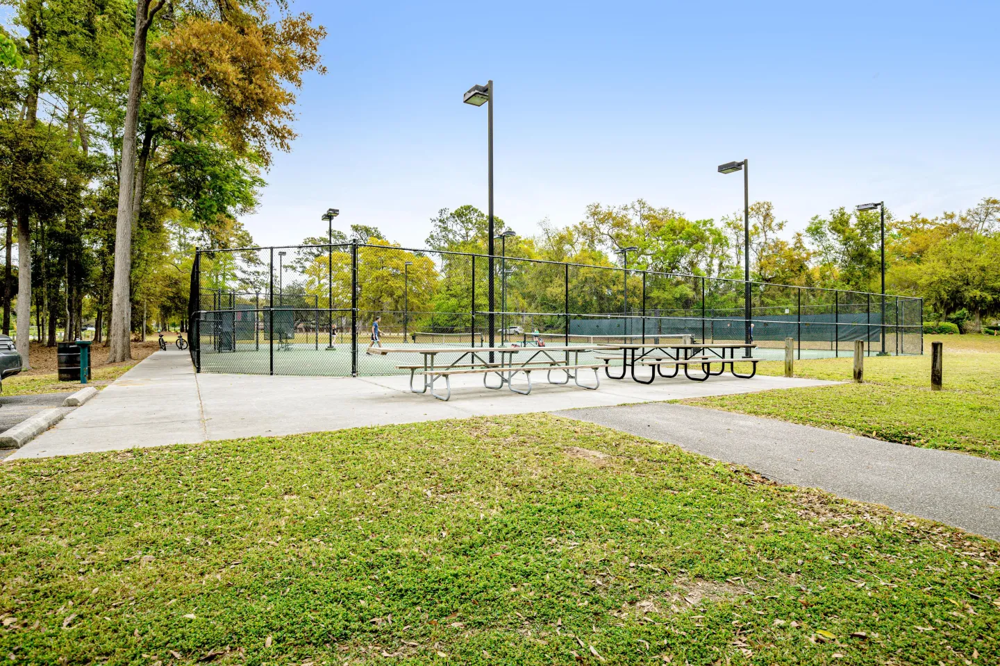Fenced outdoor tennis and sports courts surrounded by trees with picnic tables in the foreground.