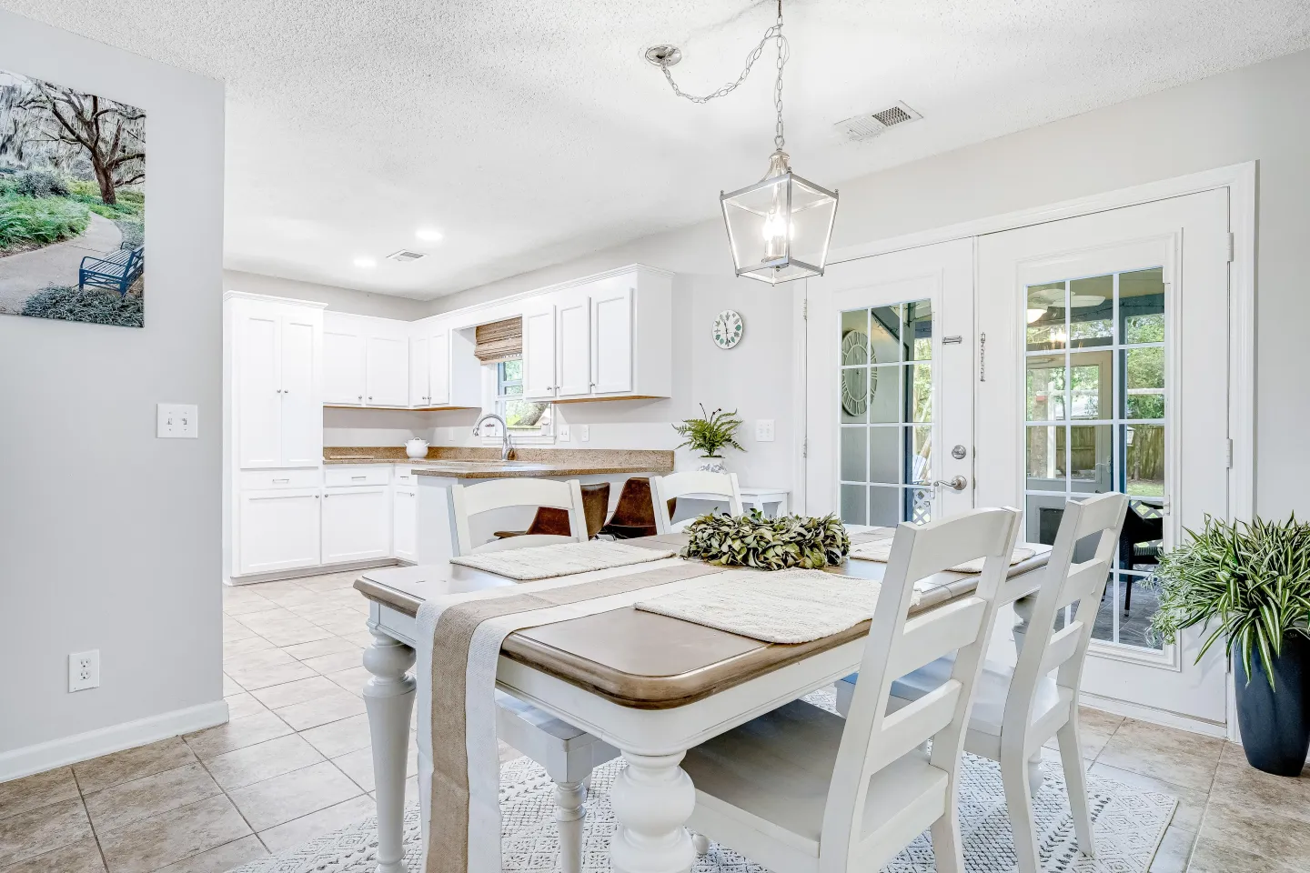 Dining area with a wooden-topped white table and chairs next to French doors and an open kitchen.