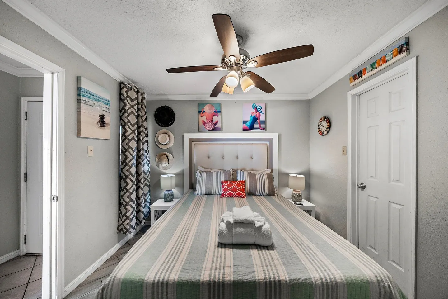 Bedroom featuring a made bed with a striped bedspread, white tufted headboard, nightstands with lamps, and a lighted ceiling fan overhead.