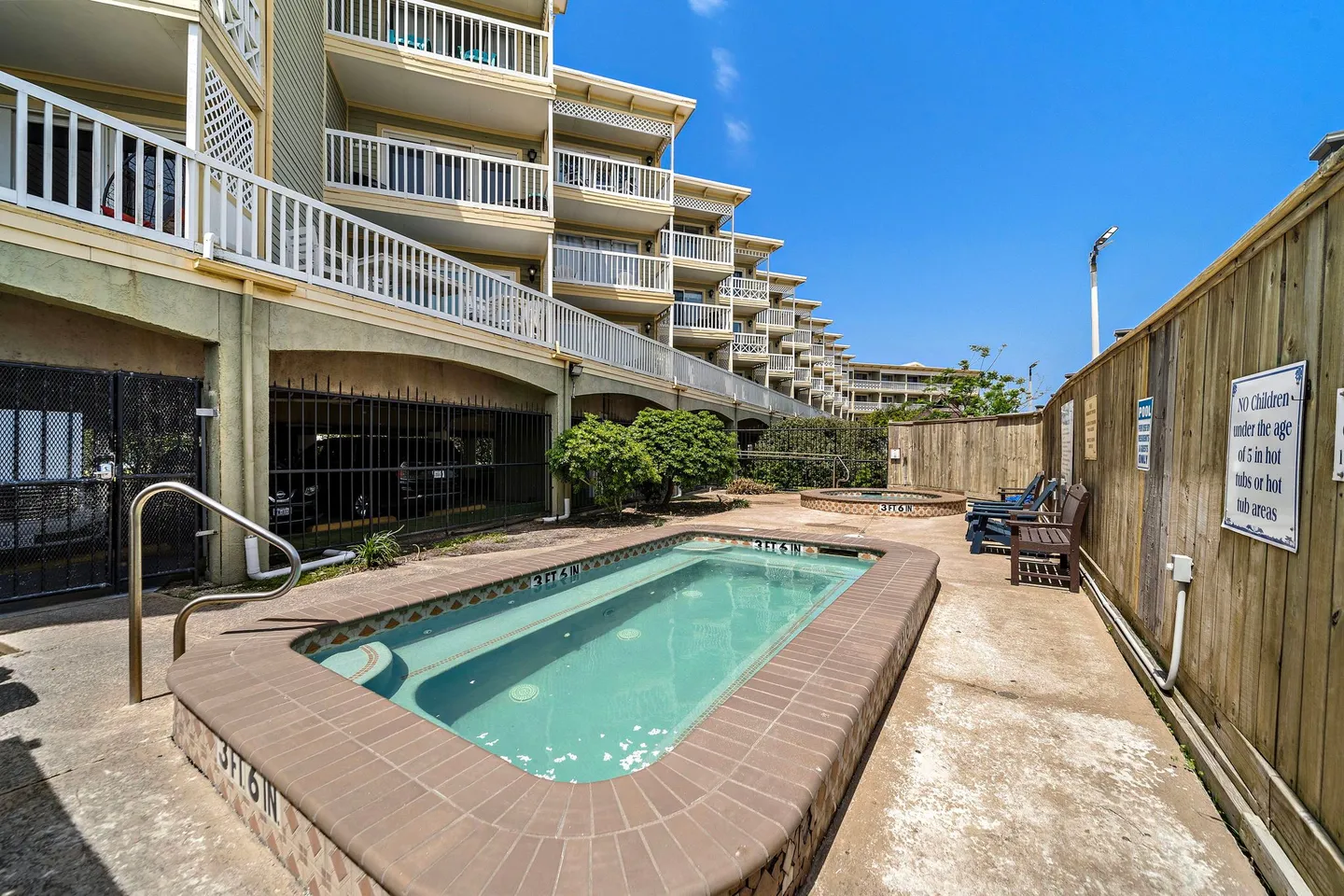 Outdoor hot tub and spa area adjacent to a multi-story condominium building with balconies.