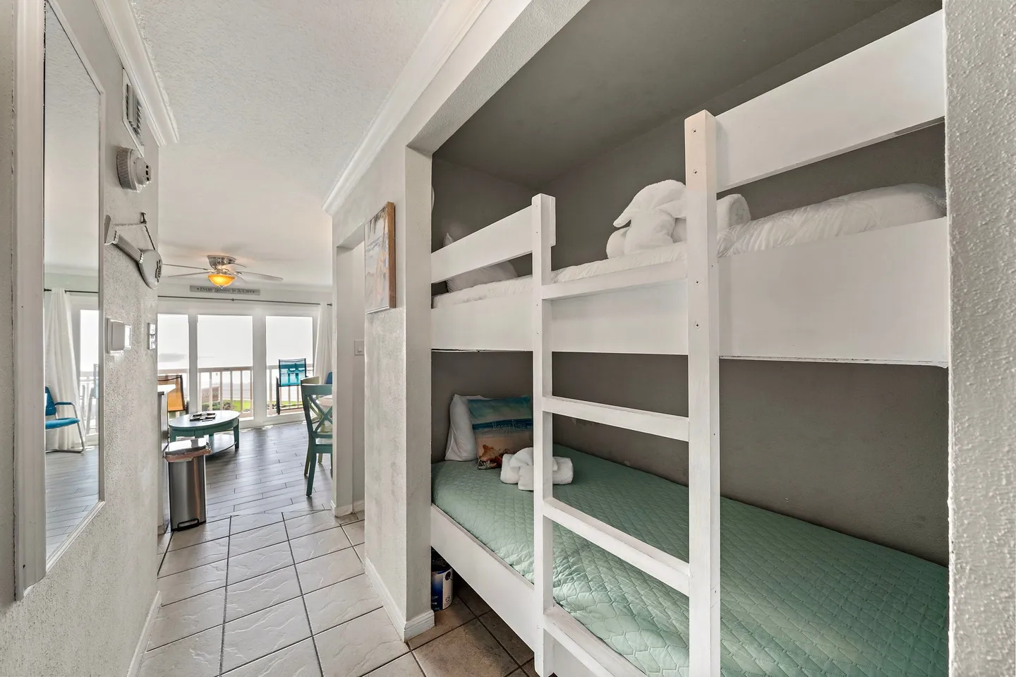Hallway alcove with built-in white bunk beds leading toward a brightly lit living area with ocean views.