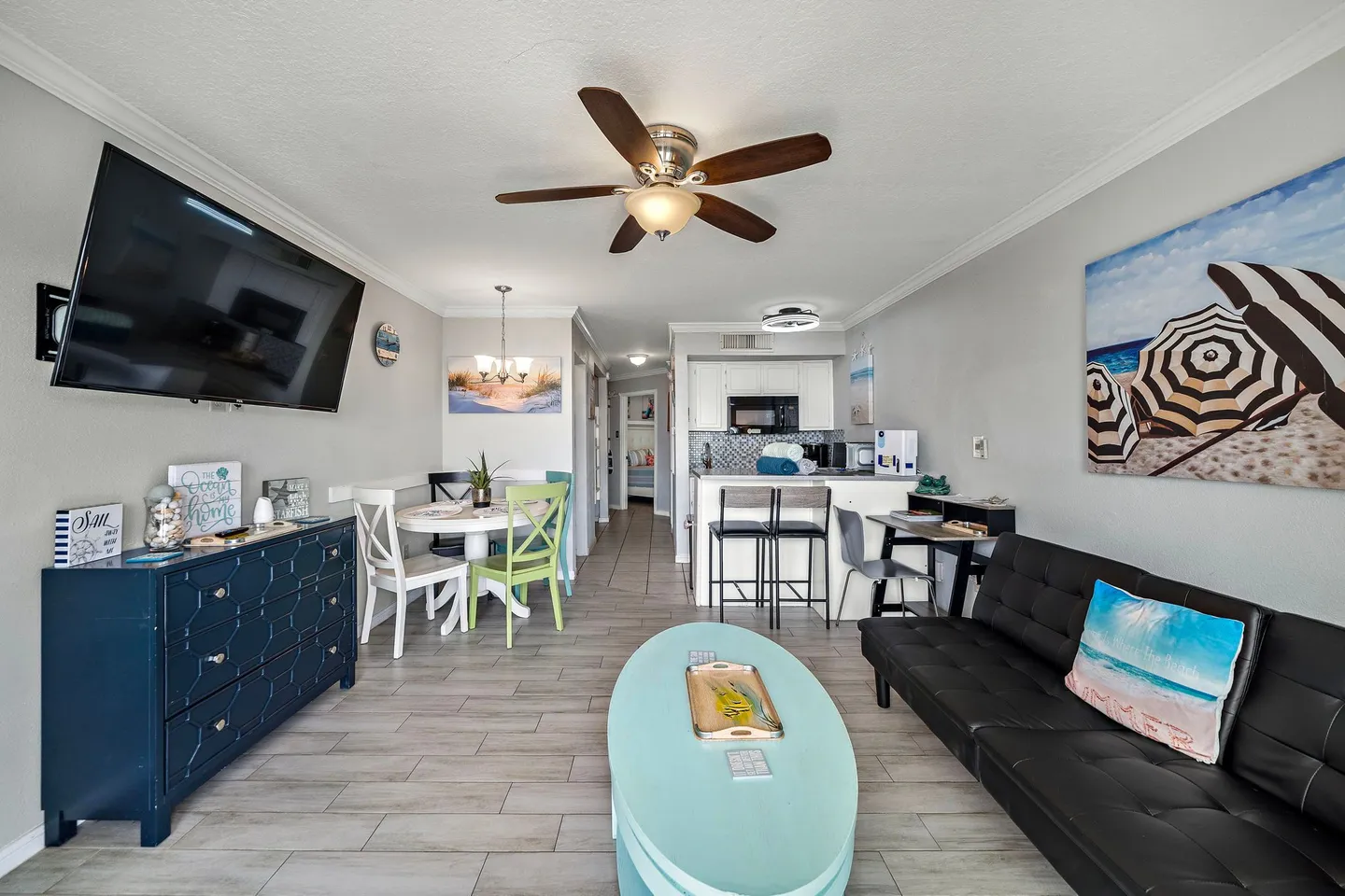 Open living area with a black sofa, light blue coffee table, dining table, and view into the kitchen.
