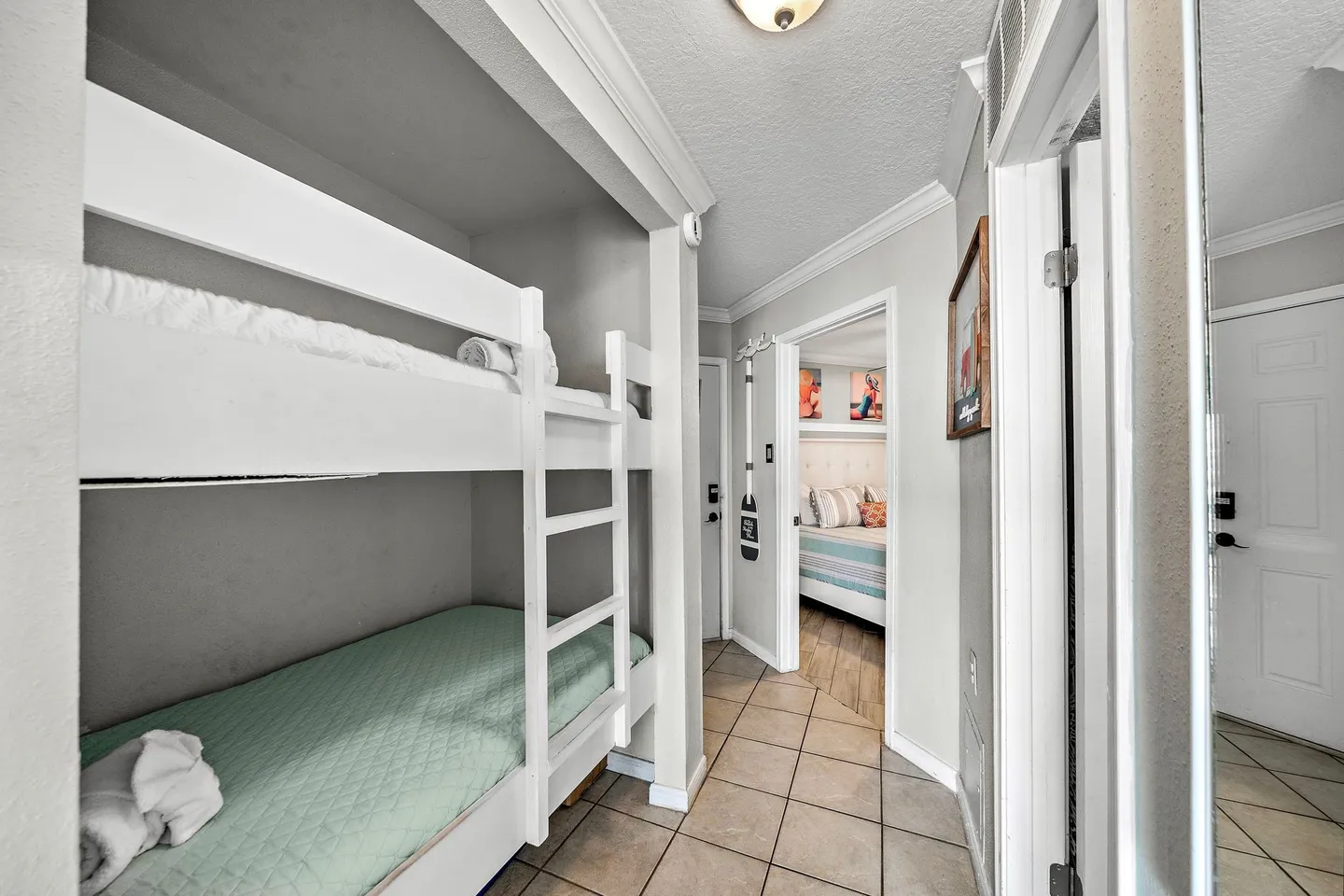 Hallway featuring built-in white bunk beds recessed into the wall with tile flooring leading to a bedroom.