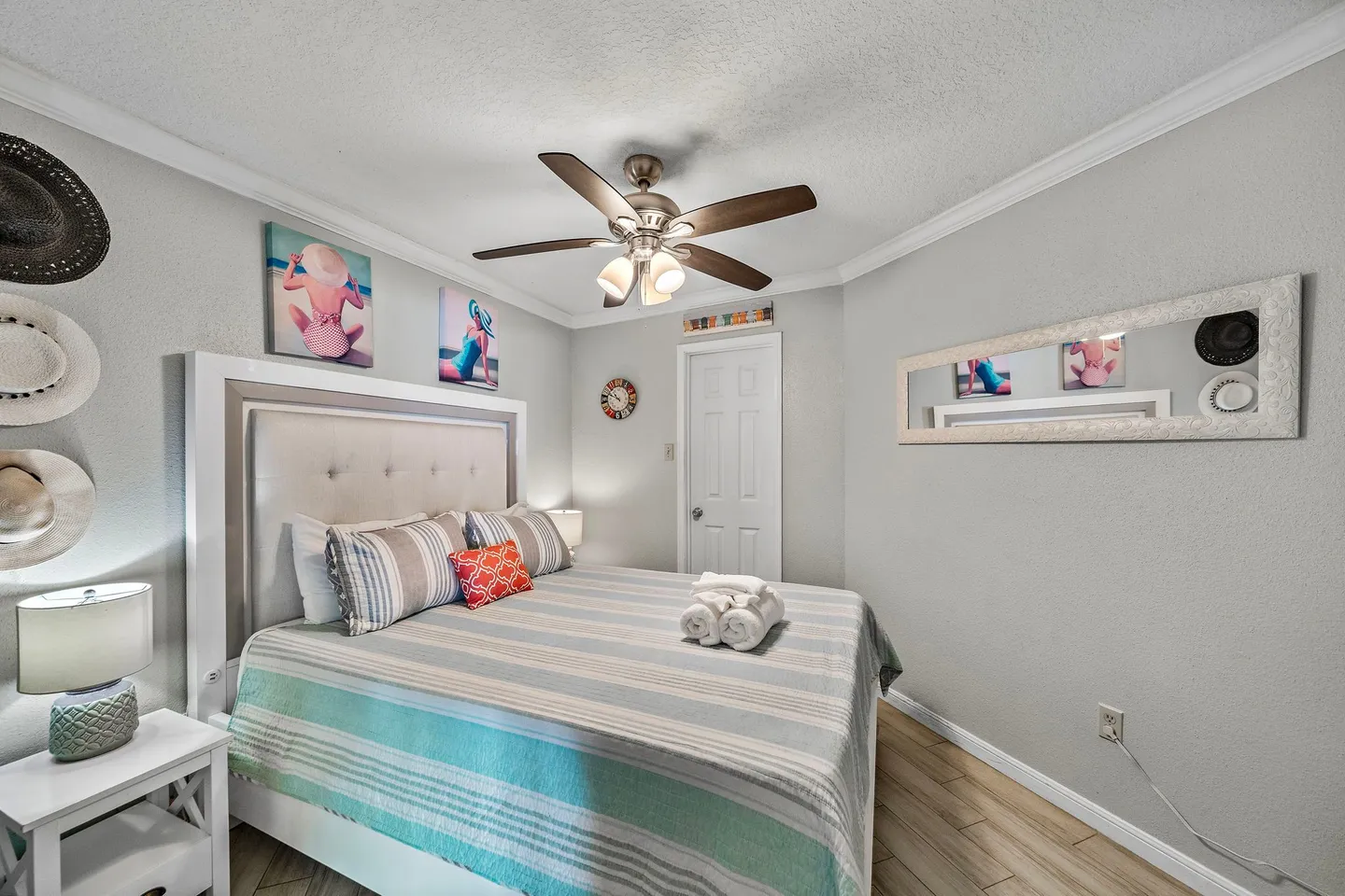 Bedroom featuring a made bed with striped bedding, a ceiling fan, beach-themed wall art, and light wood-look flooring.