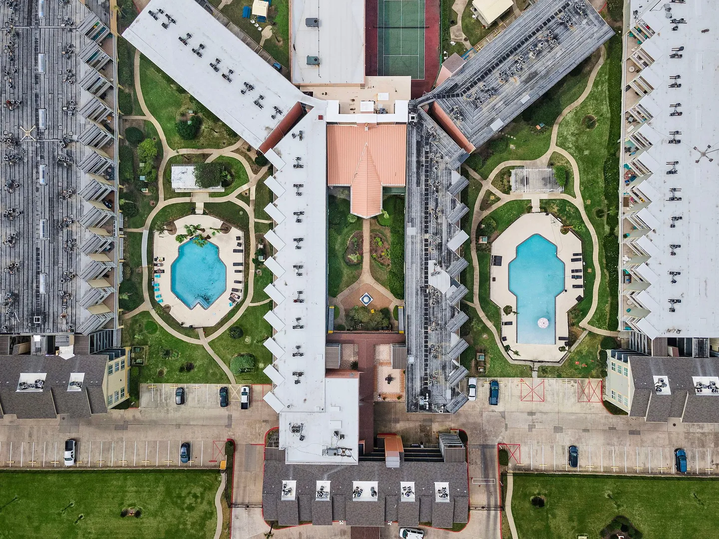 Aerial overhead view of an apartment or condominium complex featuring two swimming pools, courtyards, landscaped walkways, and parking areas.