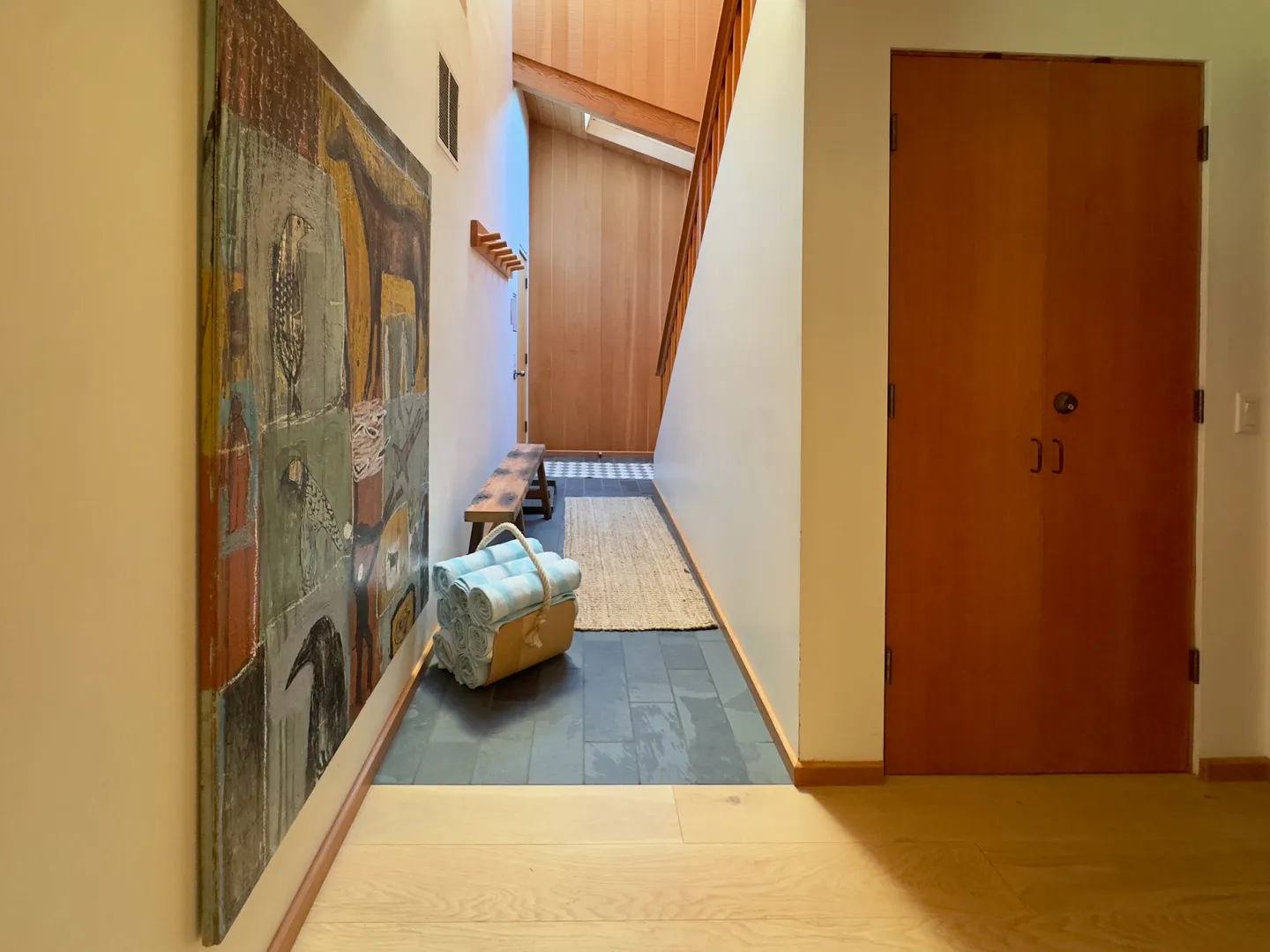 Entry hallway with slate tile flooring, light wood accents, wall art, and a basket of rolled towels.