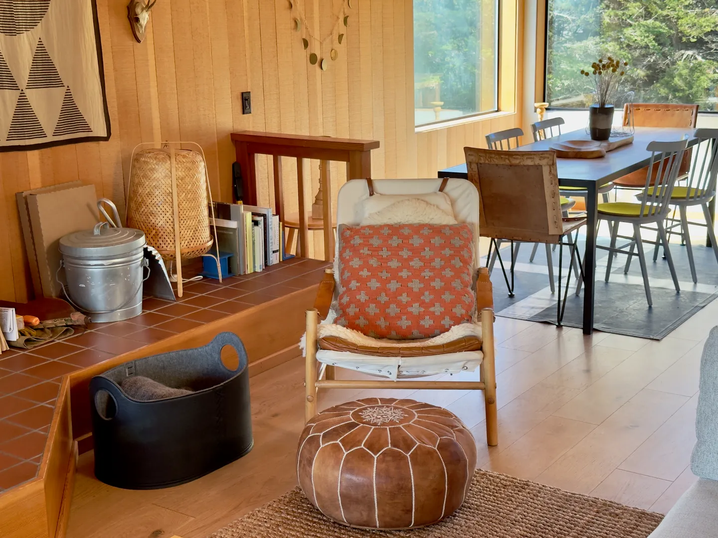Living room seating area with an armchair, leather pouf, and dining table visible in the background against wood-paneled walls.