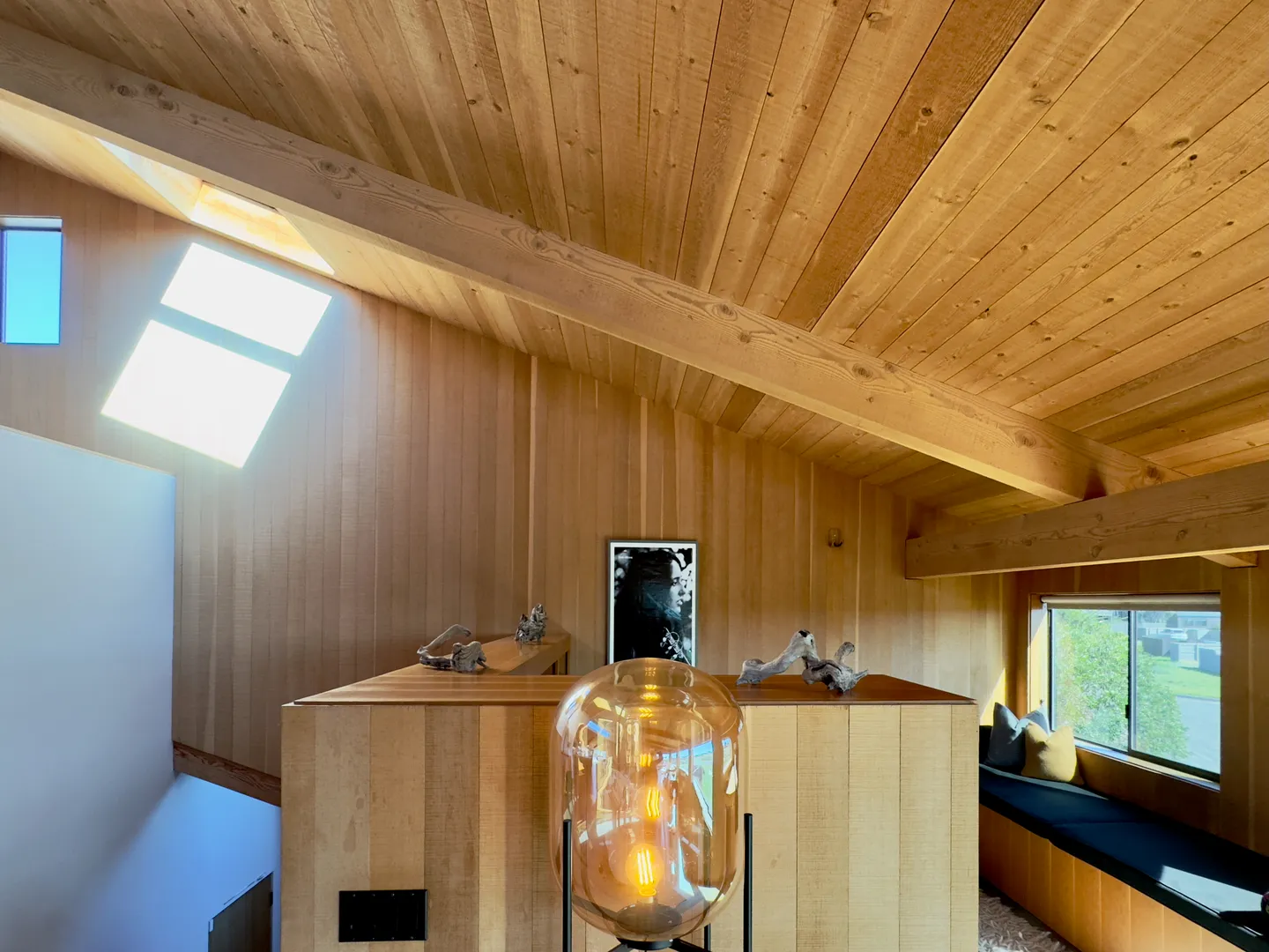 Upstairs loft area featuring wood-paneled walls, an angled wood-plank ceiling with exposed beams, skylight, and a glass floor lamp.