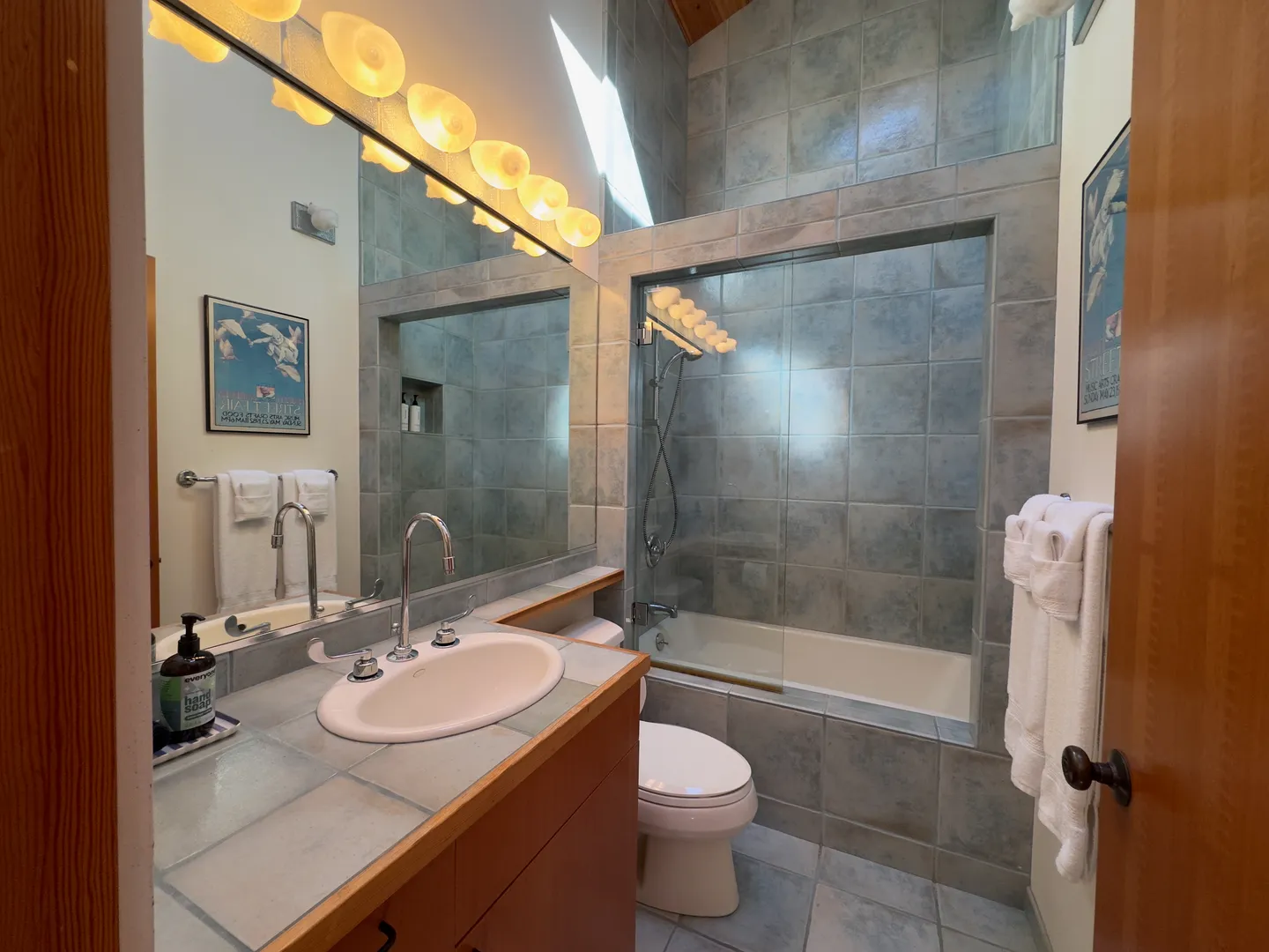 Bathroom featuring a tiled vanity with an oval sink, a toilet, and a tiled tub-shower combination with glass splash guard.