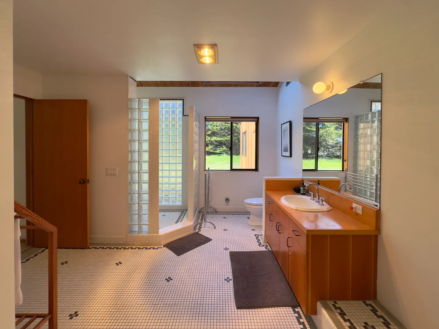 Spacious bathroom featuring a wooden vanity, a walk-in shower with glass block walls, and tiled flooring.