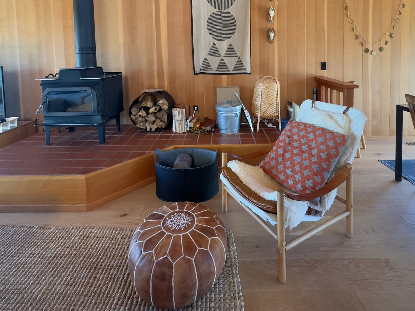 Living area featuring a wood-burning stove on a raised tiled hearth, an armchair with a patterned pillow, and a leather pouf.