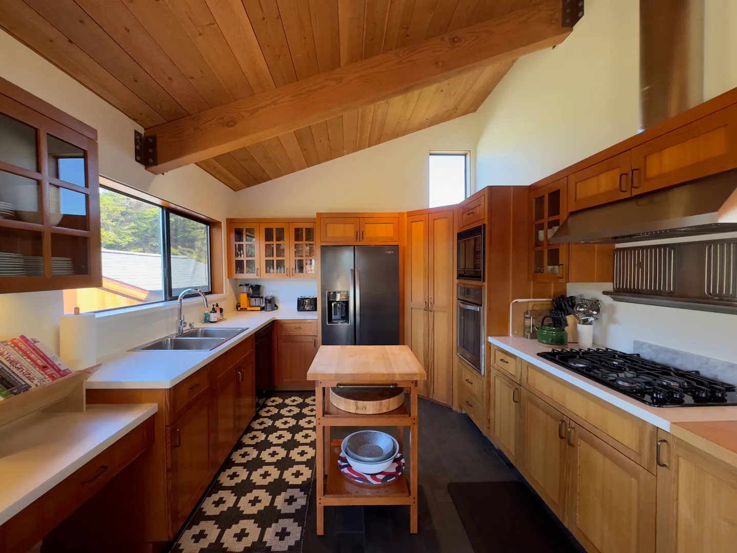 Kitchen with wooden cabinetry, vaulted wood plank ceiling, exposed beams, and a small central island cart.