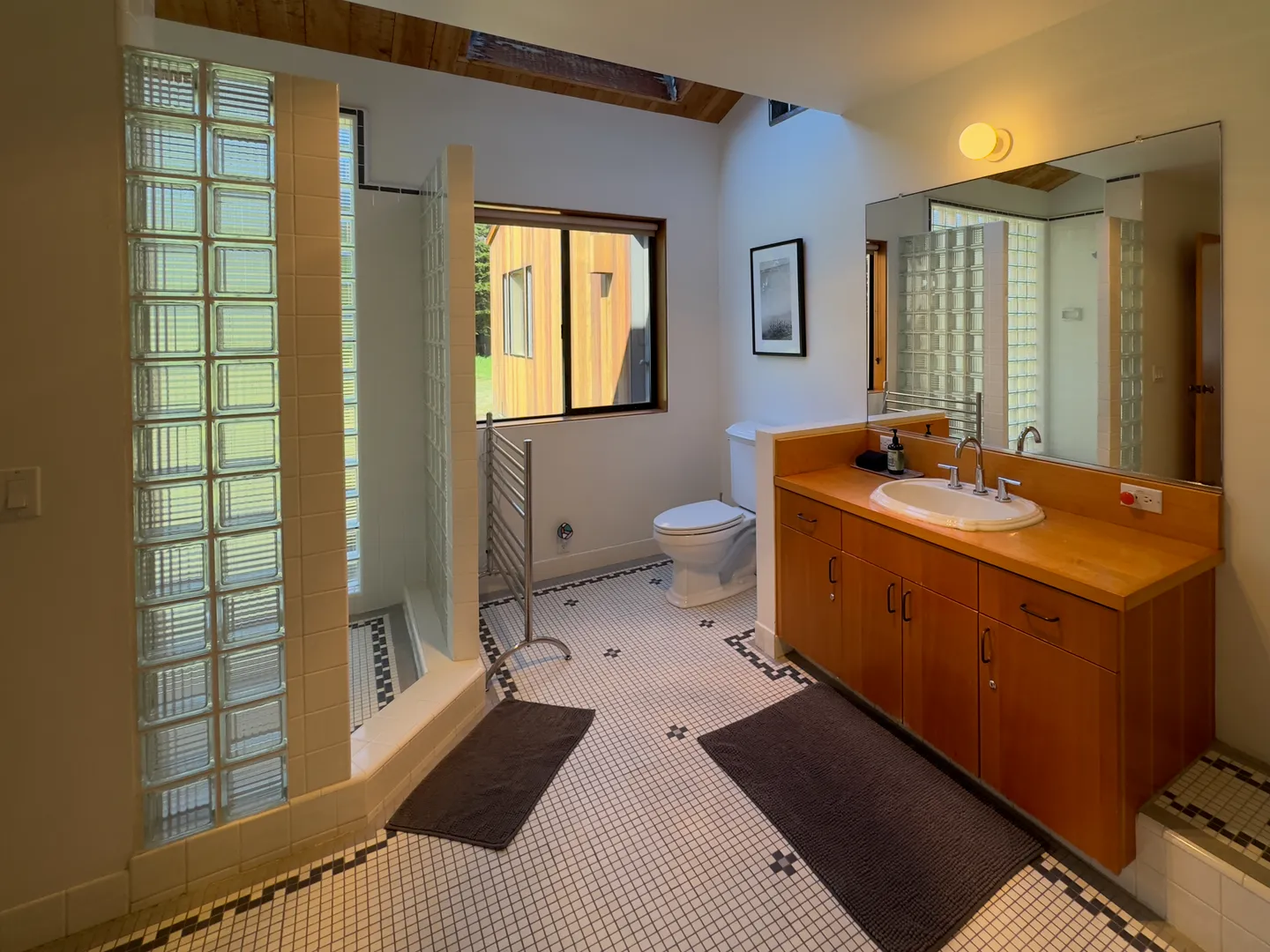 Bathroom with glass block shower wall, wood vanity, tiled floor, toilet, and window.