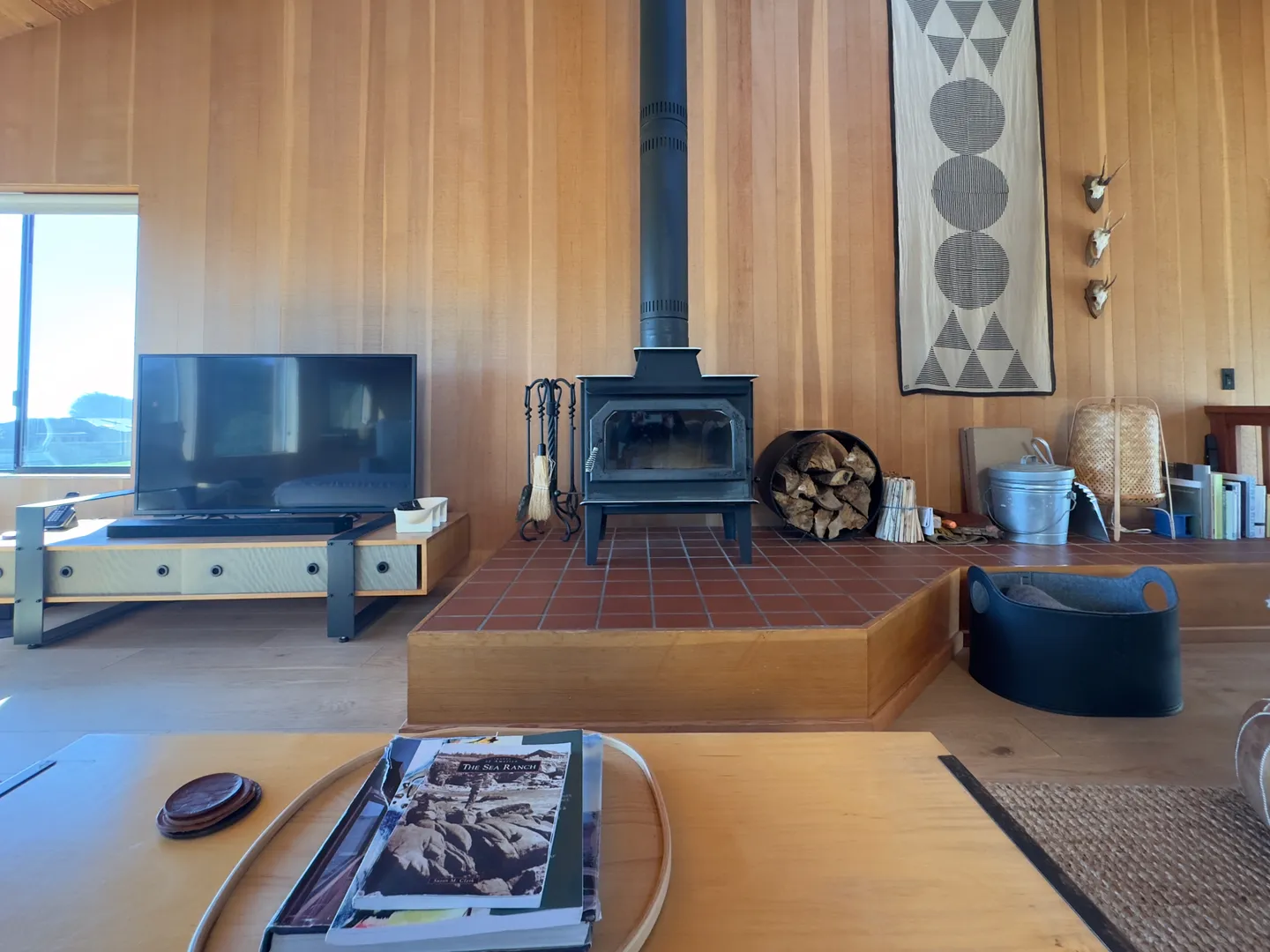Living room with wood-paneled walls, a wood-burning stove on a raised tile hearth, and a television on a low media console.