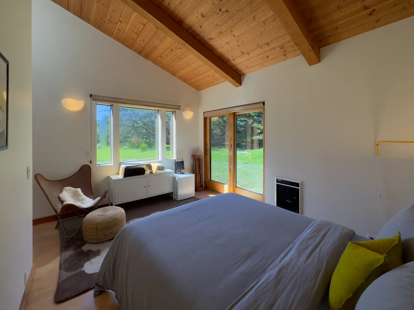 Bedroom featuring vaulted wood ceilings with exposed beams, large windows, and a sliding glass door looking out to a grassy yard.