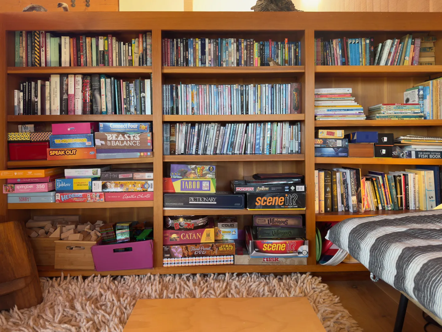 Built-in wooden bookcase filled with books, movie cases, and board games next to a striped seat and shag rug.