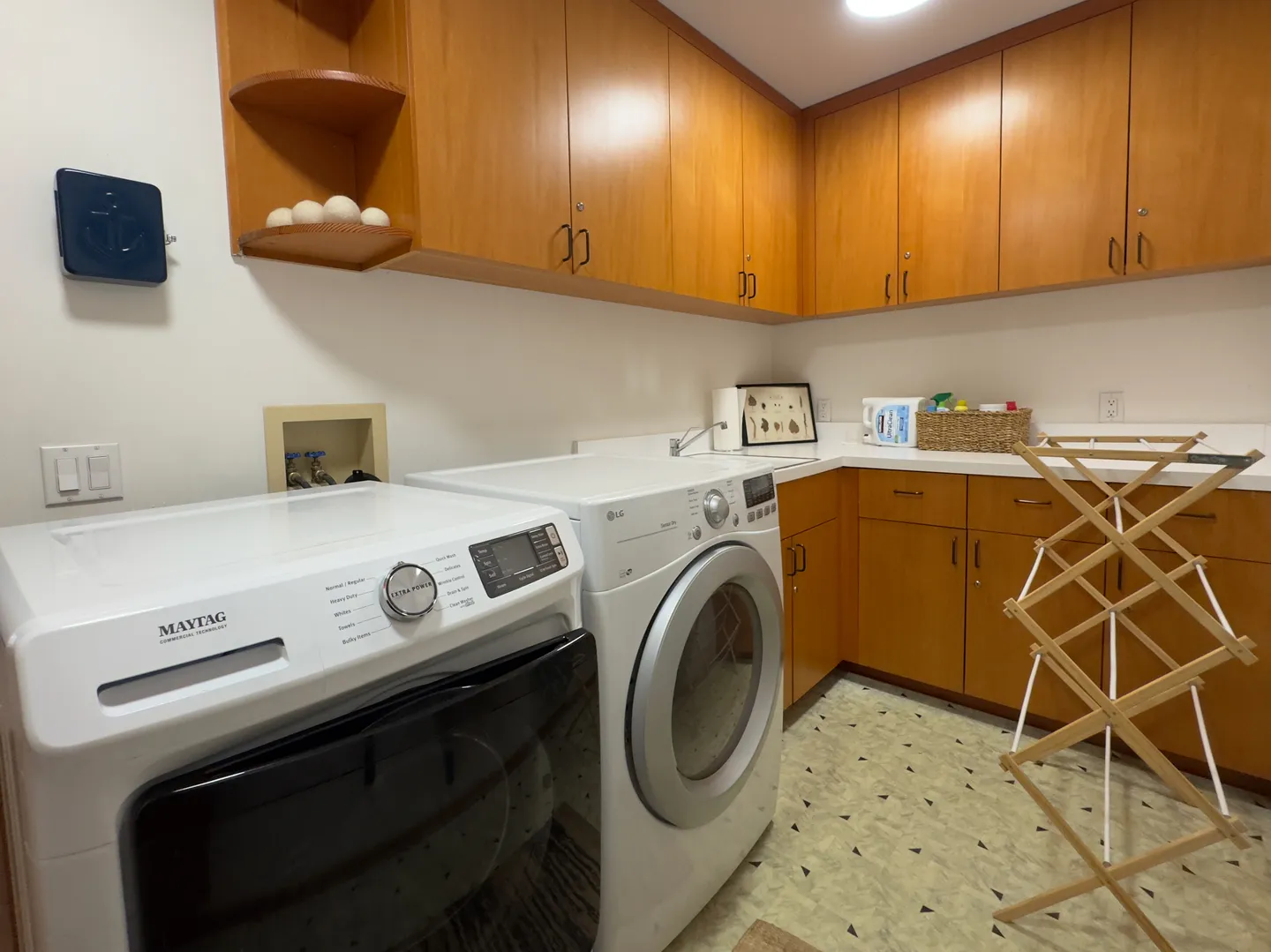 Dedicated laundry room with front-loading washer and dryer, wooden cabinetry, and a folding drying rack.