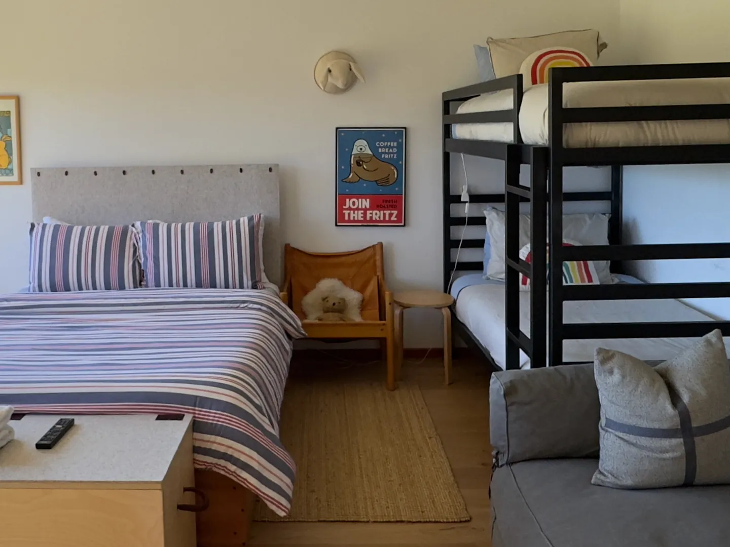 Bedroom with a bed dressed in striped bedding, a dark metal bunk bed, an accent chair, and a grey sofa corner.