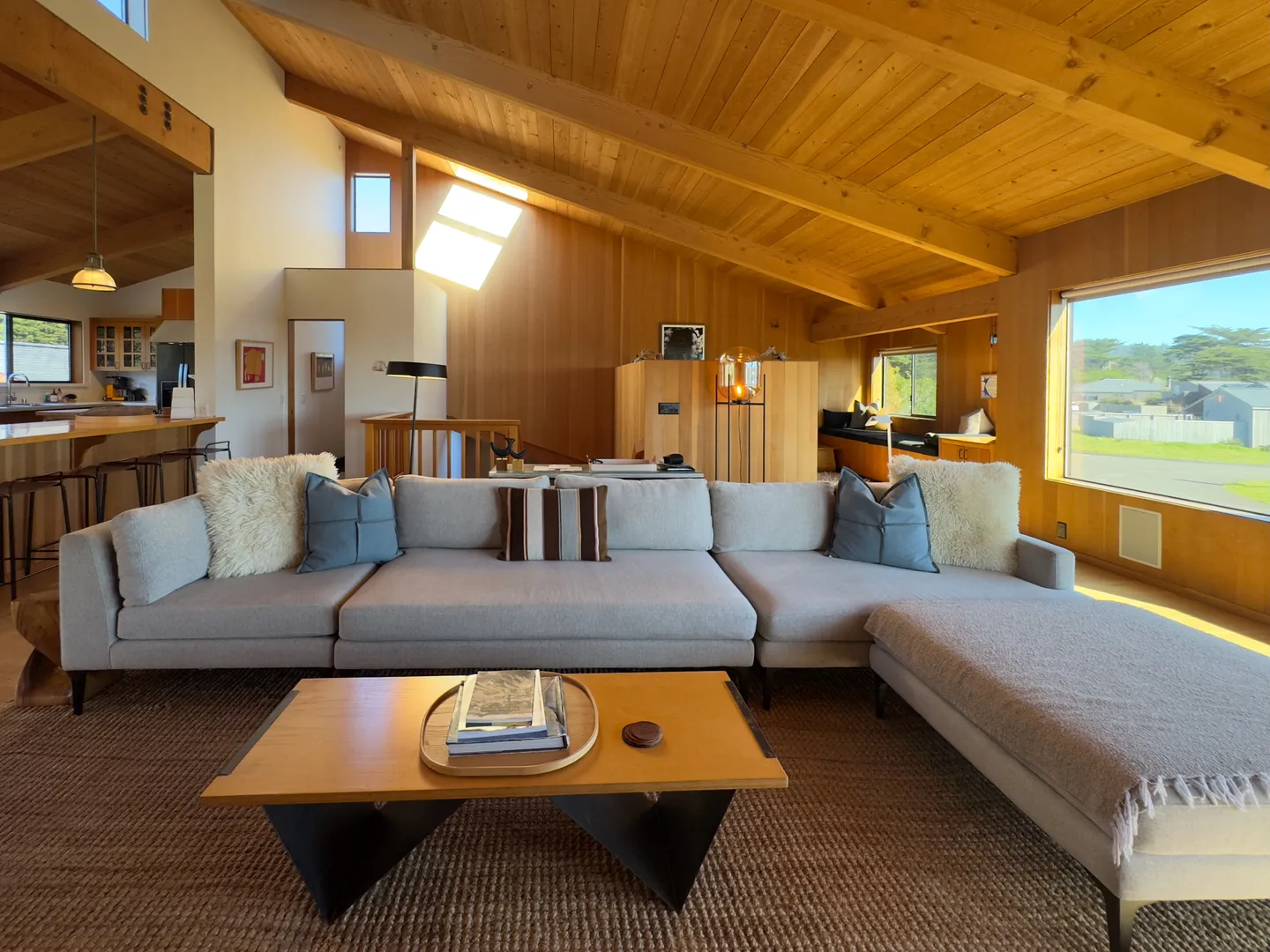Open-concept living room with wood-paneled vaulted ceiling, large gray sectional sofa, coffee table, and large window.