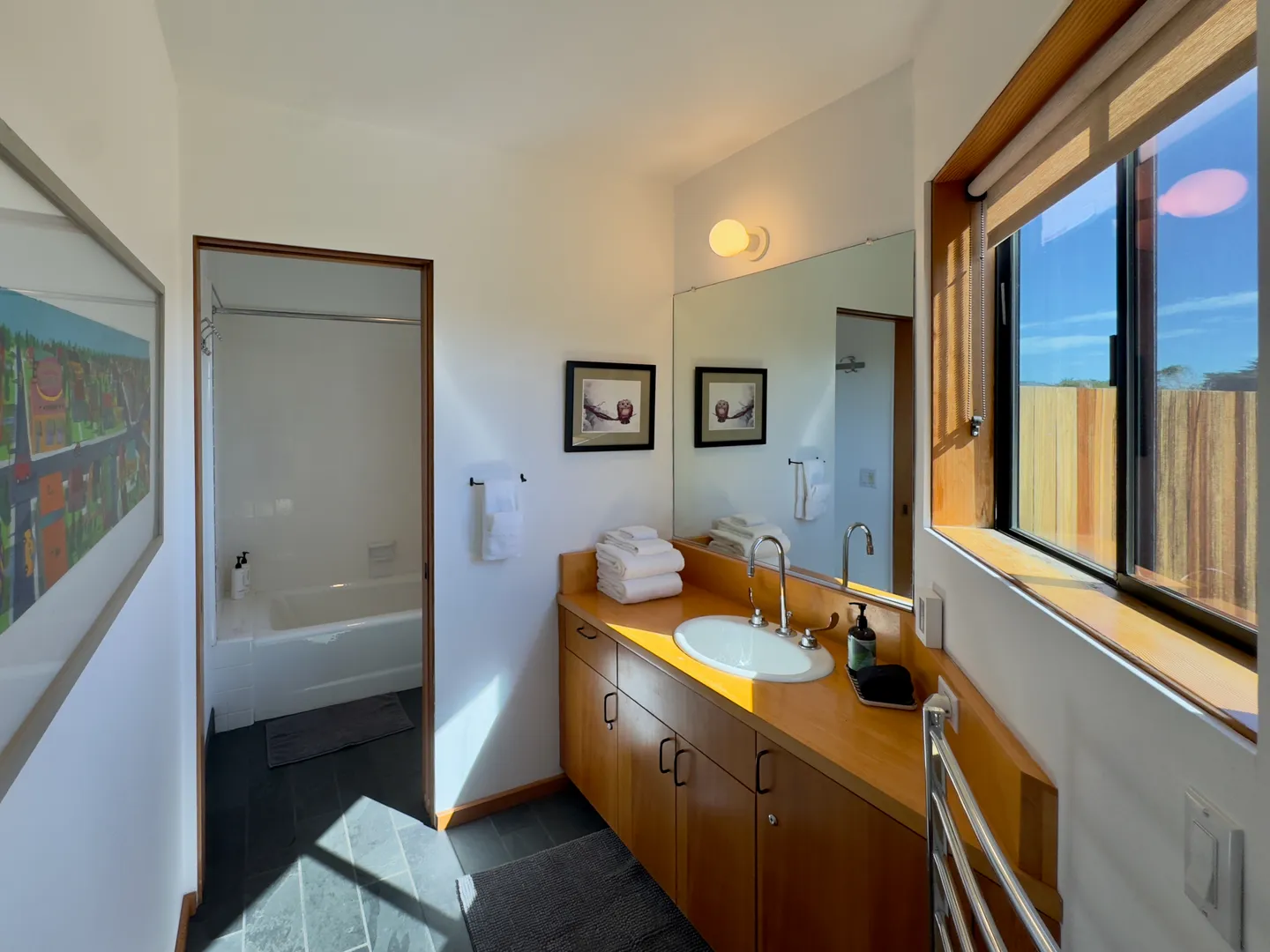 Bathroom with wooden vanity, oval sink, large mirror, slate-tiled floor, and doorway to a bathtub and shower enclosure.