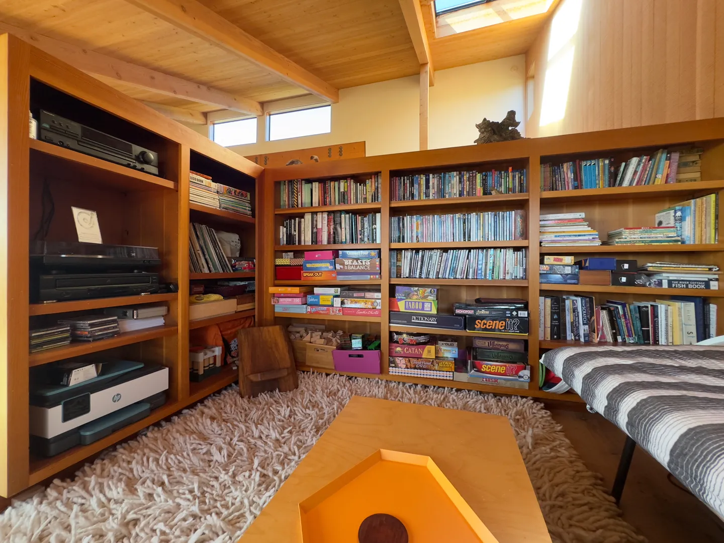 Cozy reading and entertainment nook with wood bookshelves filled with books, board games, media, and a low table on a shag rug.