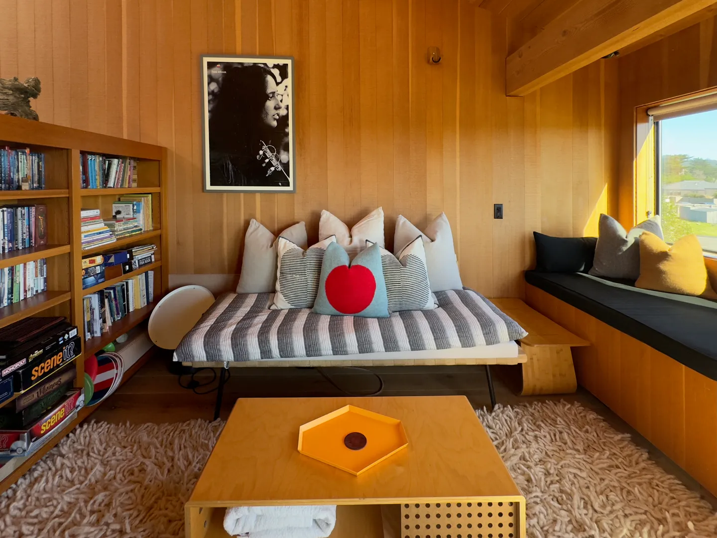 A cozy wood-paneled sitting room with a daybed, pillows, coffee table, and full bookcase.