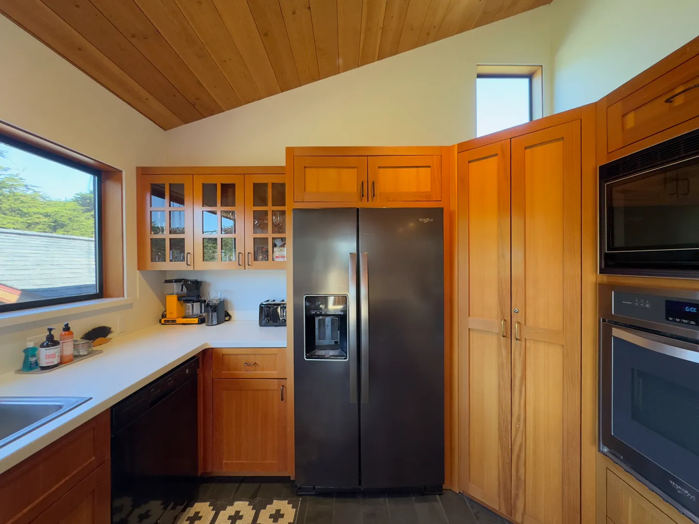 Kitchen corner featuring wood cabinetry, stainless-steel appliances including a refrigerator and wall ovens, and a sloped wood-paneled ceiling.