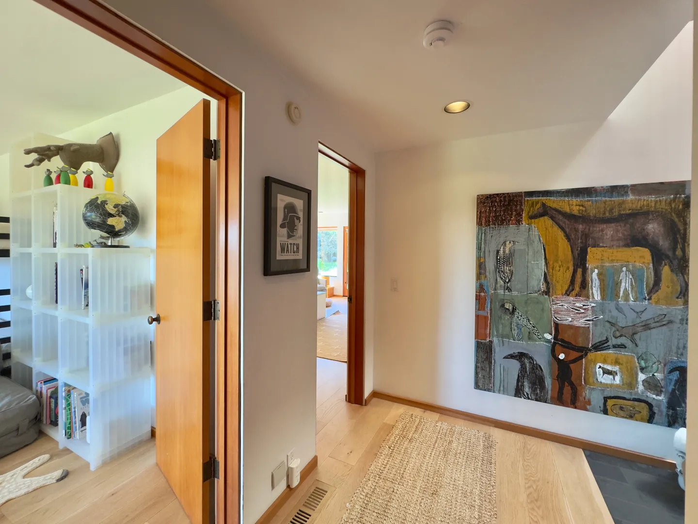 Hallway with light wood floors featuring large artwork on the wall, leading to adjacent rooms.