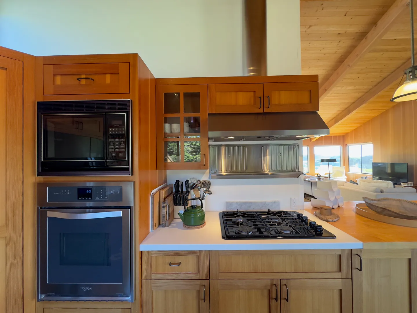 Kitchen cooking area with wood cabinets, built-in wall oven, microwave, gas cooktop, and stainless steel vent hood.