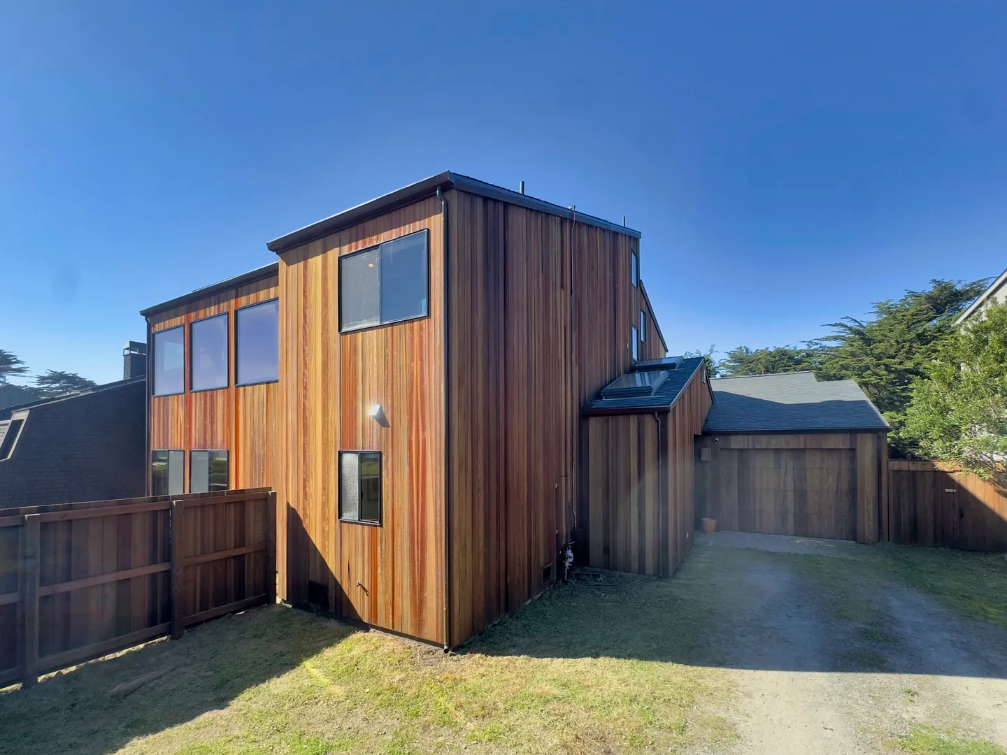 Exterior view of a multi-story home with vertical wood siding under a clear blue sky.
