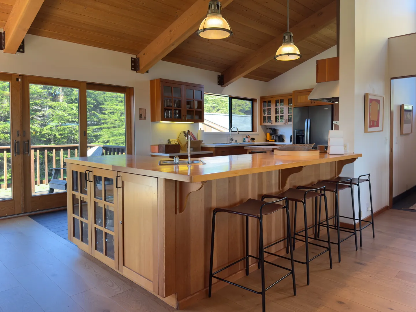 Kitchen with wood island, bar stools, exposed-beam vaulted ceiling, and sliding glass door leading to a deck.