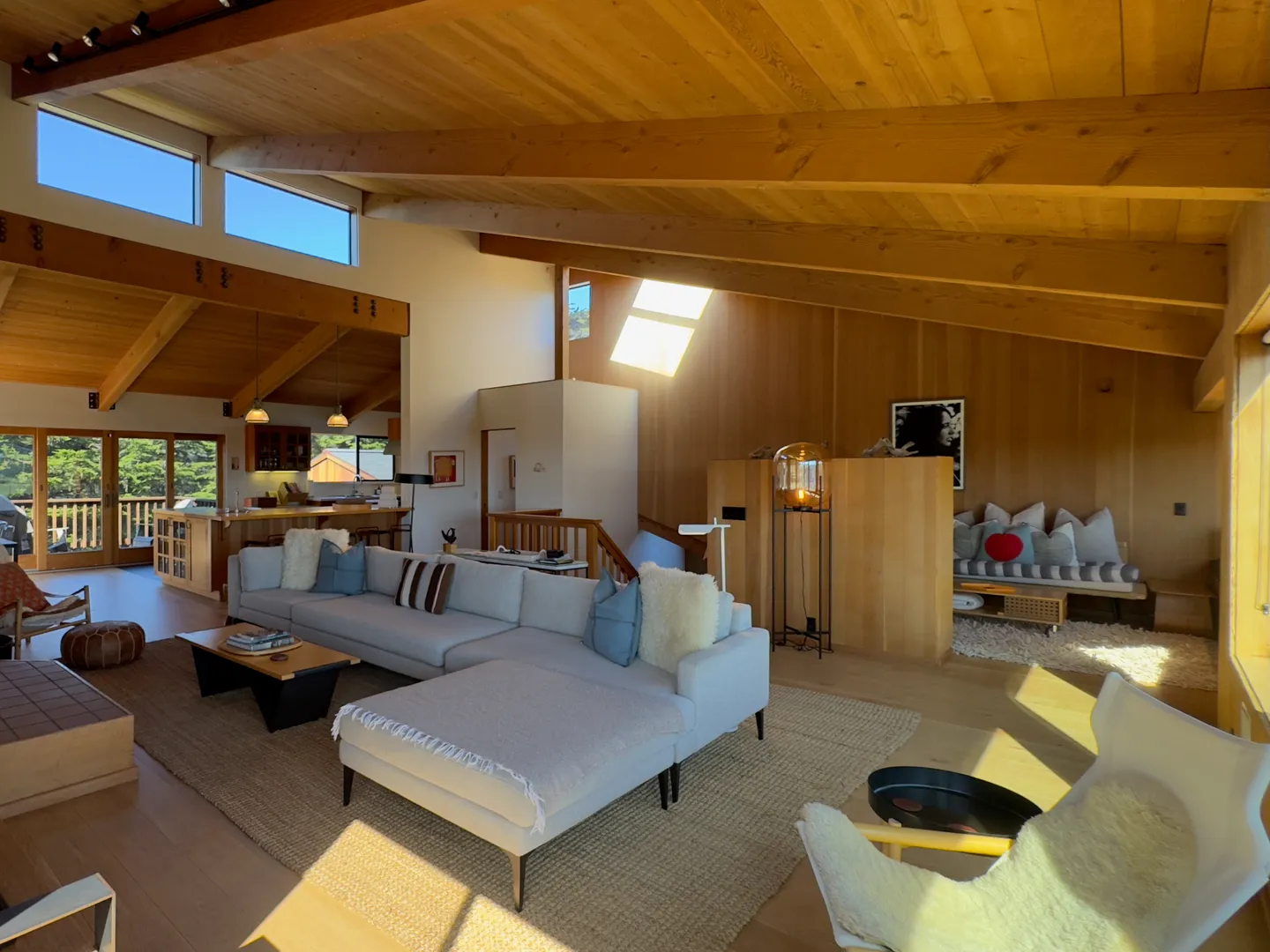 Open-concept living room with wood-paneled sloped ceiling, sectional sofa, and kitchen in the background.