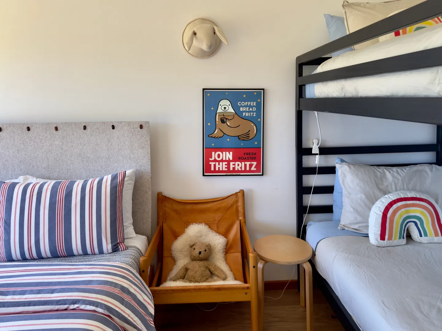 Bedroom featuring a bed with a striped duvet, a leather sling chair with a teddy bear, a wooden side table, and a black bunk bed.