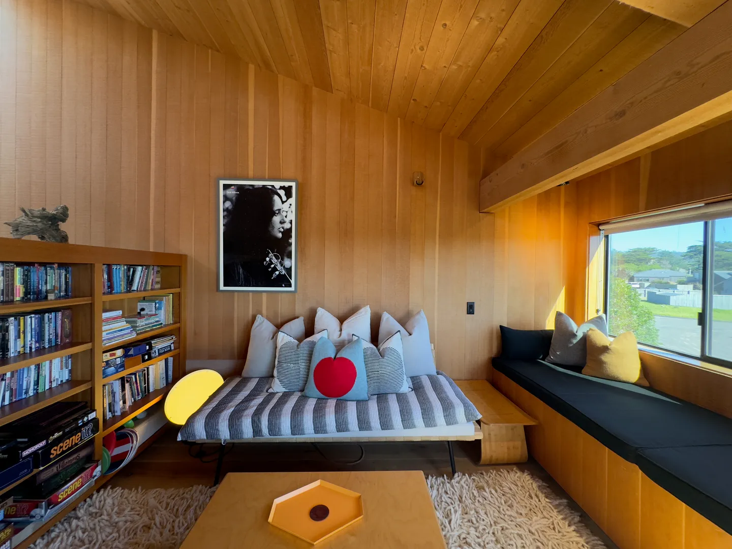 Cozy wood-paneled sitting room with a daybed, built-in window seat, bookshelf, and shag rug.