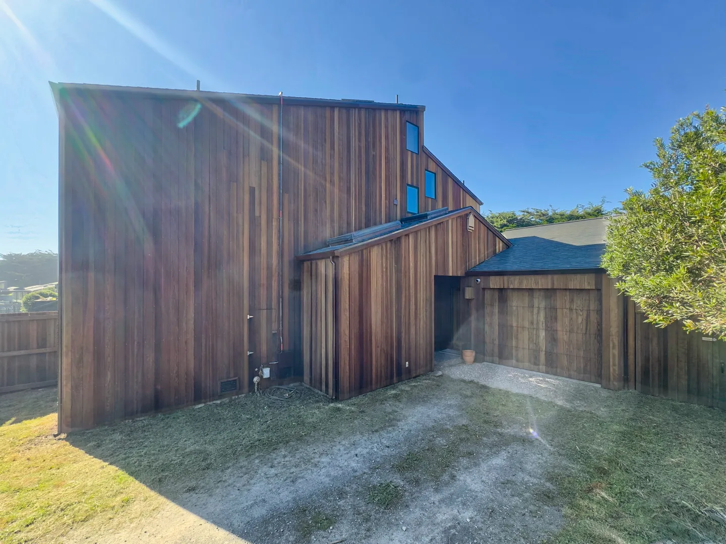 Exterior view of a multi-story home with vertical wood siding under a clear blue sky.
