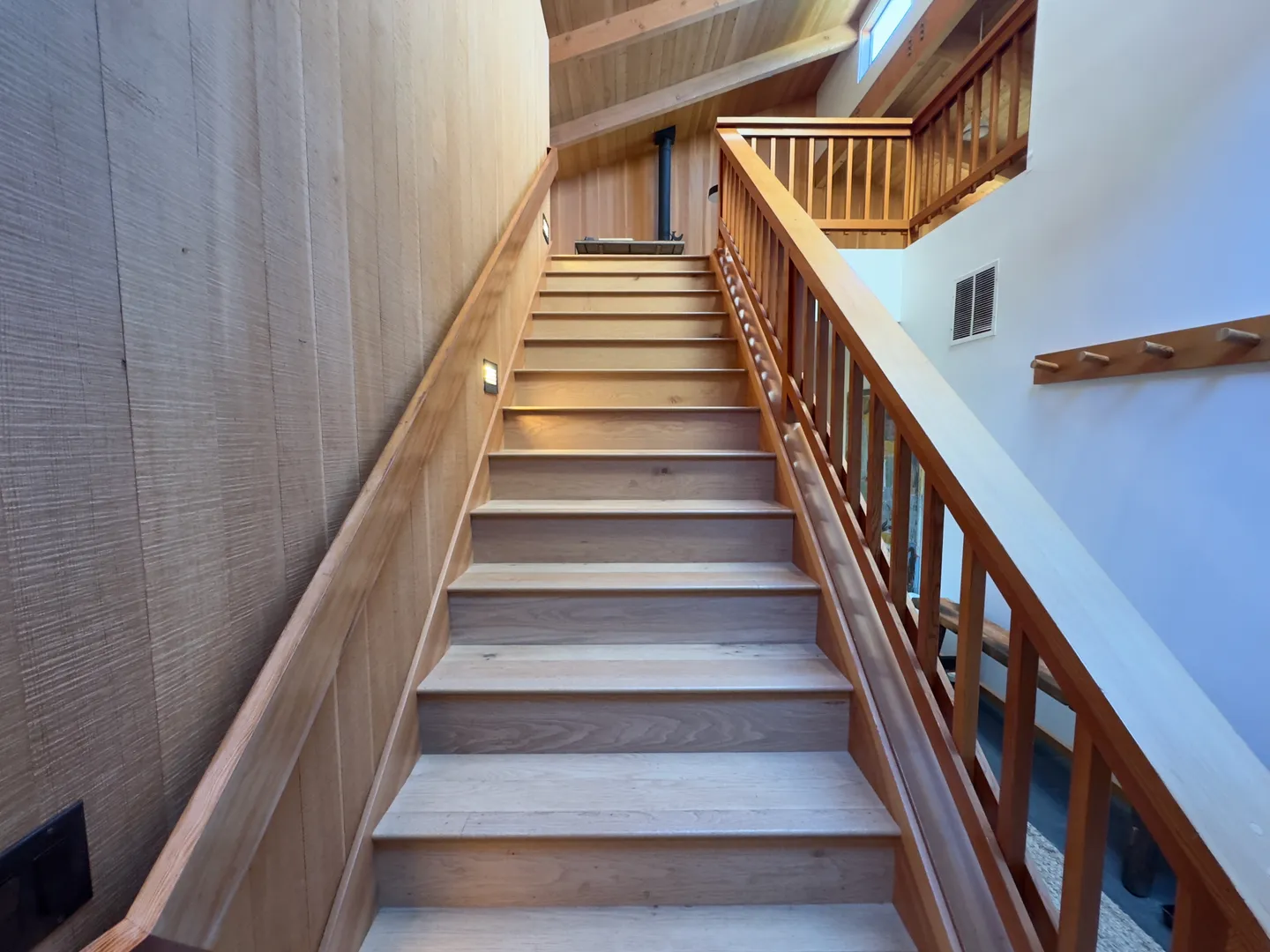 Upward view of a wooden staircase with matching wood railings and wood-paneled walls.
