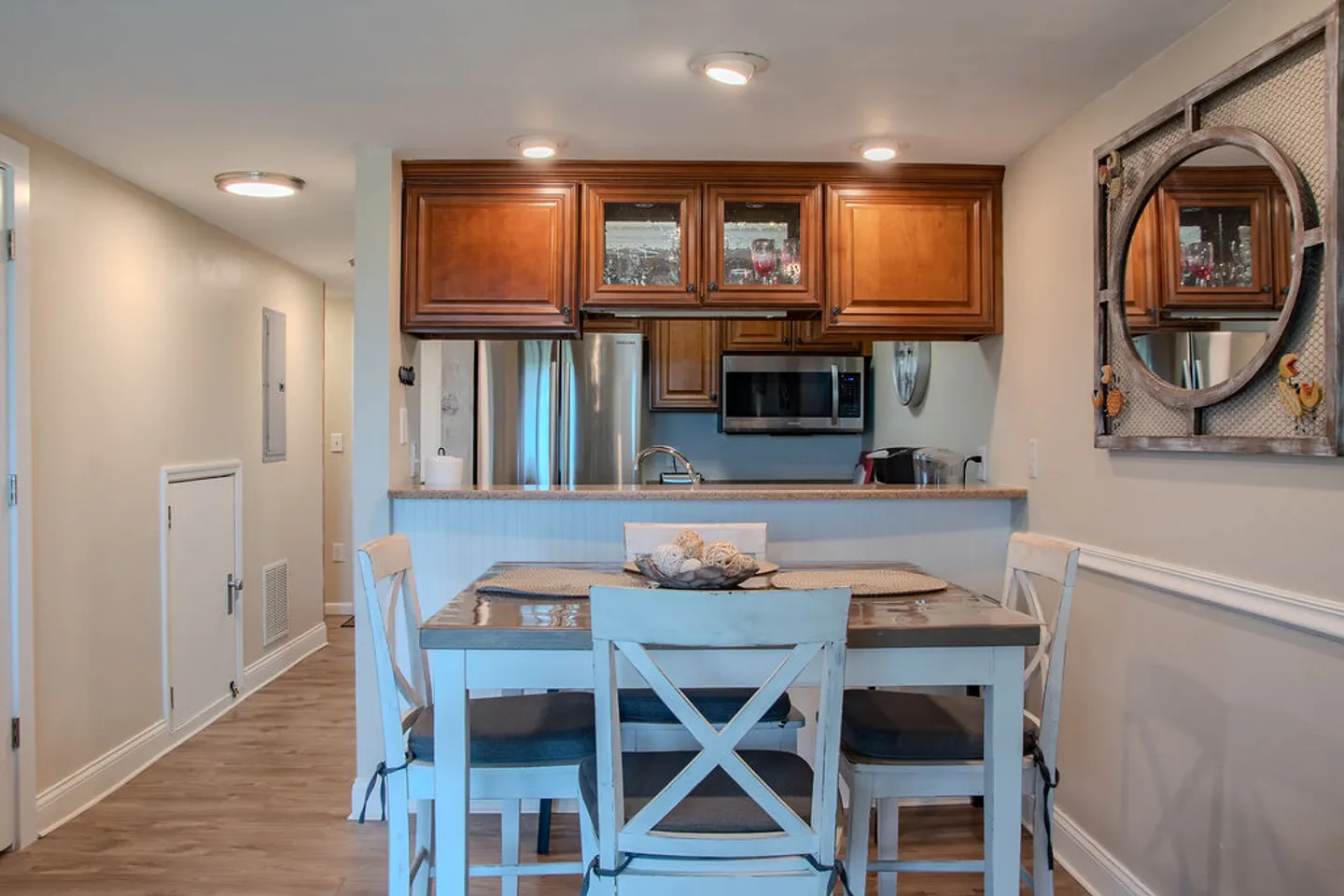 Dining area with a wooden table and white cross-back chairs positioned in front of a pass-through kitchen counter.