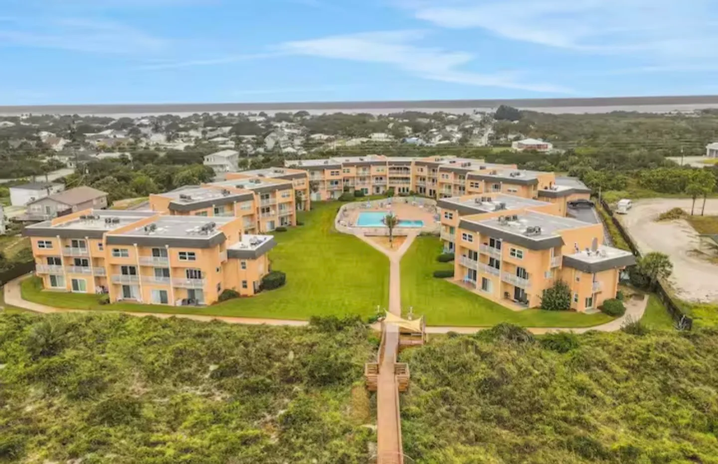 Aerial view of a peach-colored condominium complex surrounding a central courtyard with a swimming pool and boardwalk access.