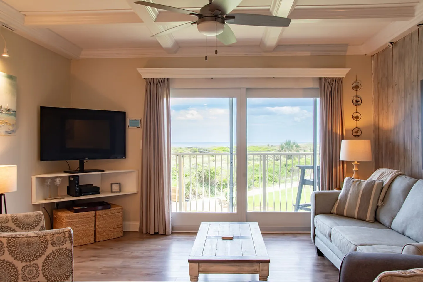 Living room with a sofa, coffee table, TV, and sliding glass doors leading to a balcony with coastal views.