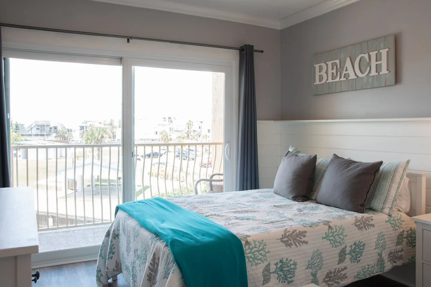 Bedroom with coastal bedding next to sliding glass doors leading to a balcony.