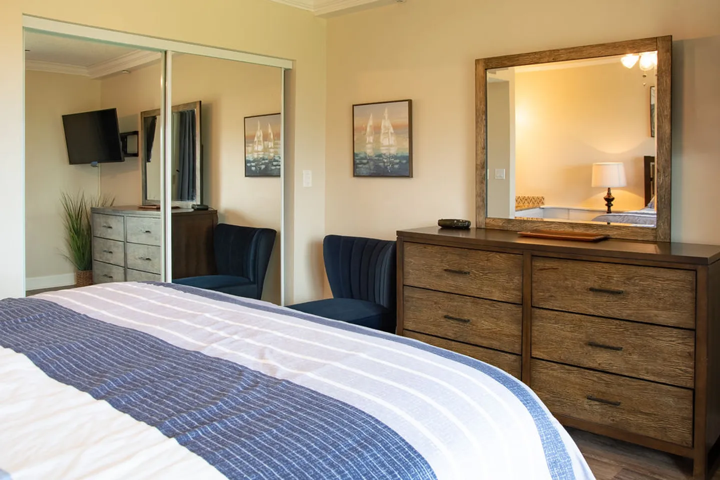 Bedroom featuring a bed with a blue and white striped blanket, a wooden dresser with a mirror, and mirrored sliding closet doors.
