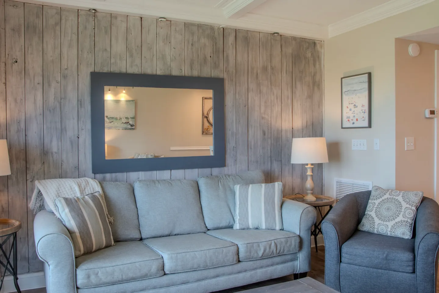 Living area with a light grey sofa, an armchair, and a horizontal framed mirror set against a weathered wood-paneled accent wall.