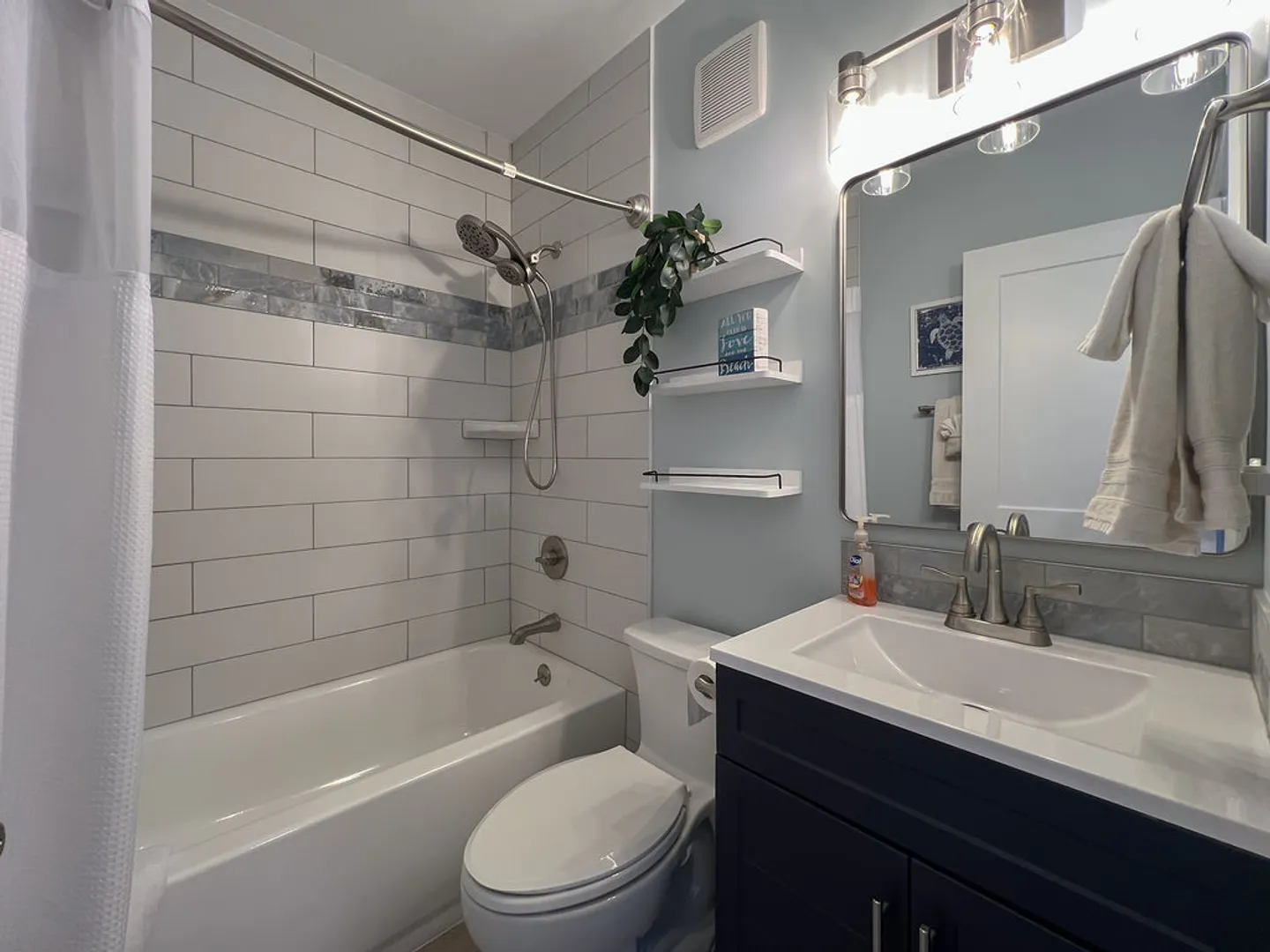 A bathroom featuring a tiled shower-tub combination, toilet, and vanity with a dark cabinet and mirror.
