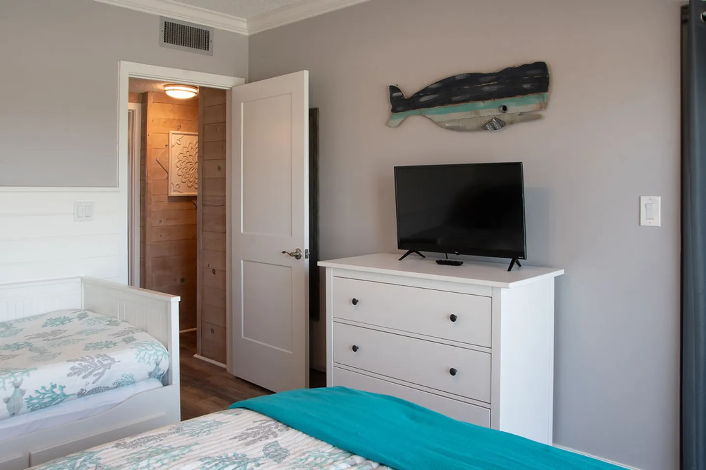 Bedroom featuring twin beds with patterned bedding, a white dresser with a mounted television, and rustic whale wall art.