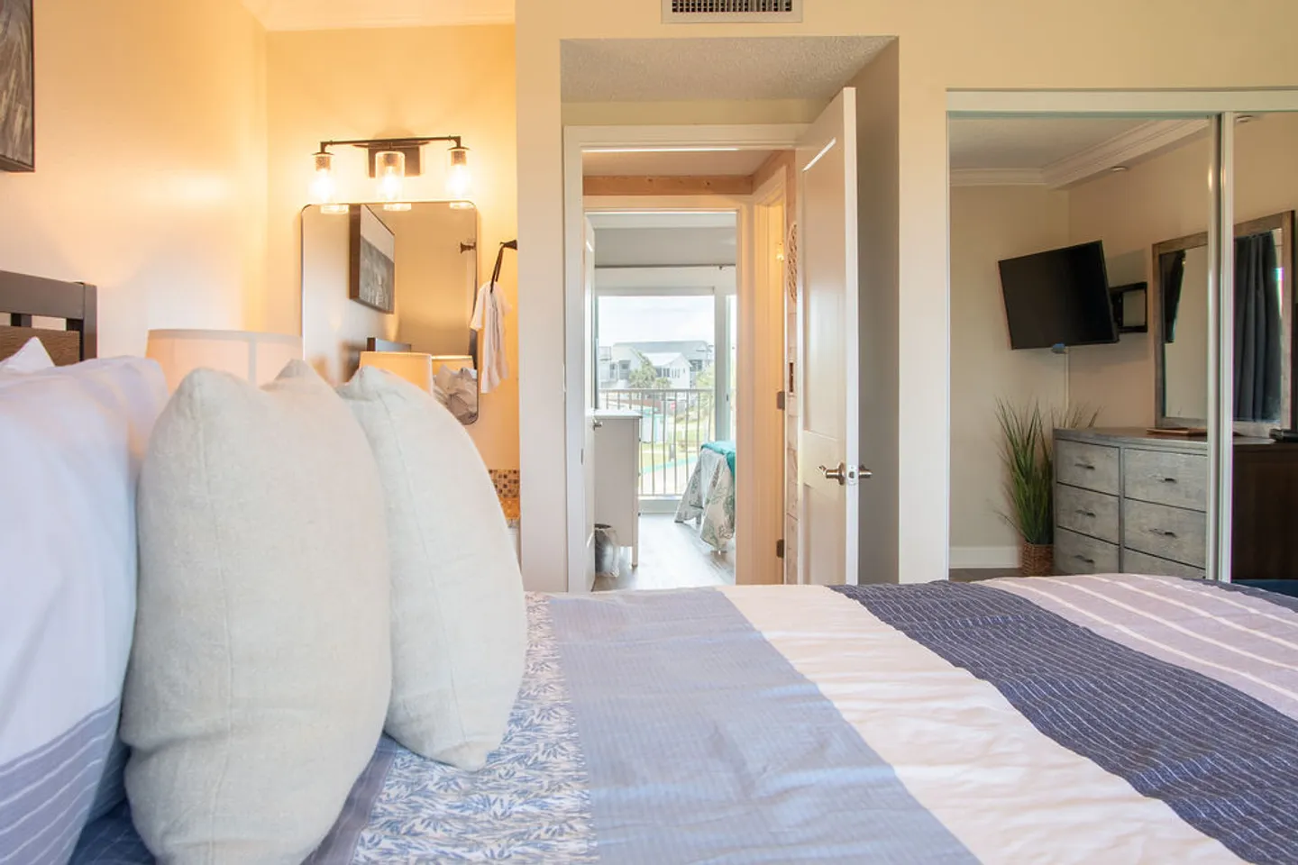 Bedroom with blue and white patterned bedding looking through a doorway toward a balcony and mirrored sliding closet doors.